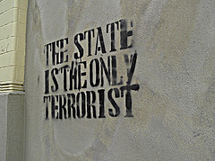 Black graffitti stenciled on a stone wall saying, THE STATE IS THE ONLY TERRORIST
